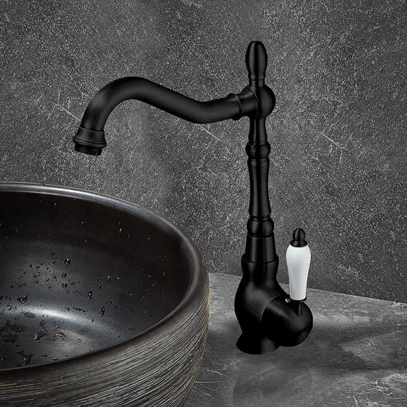 A matte black kitchen faucet with a curved spout and a white lever handle, shown installed beside a dark stone vessel sink against a textured gray wall.